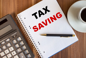 TAX SAVING written in a white notepad near a calculator and a cup of coffee on a dark wooden background