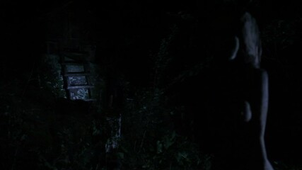 At night, a tourist with a flashlight in the forest searches for a wooden house