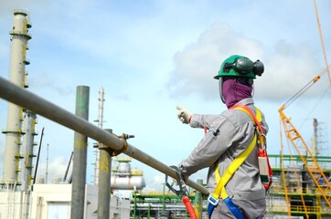 Foreman, supervisor, engineer standing on scaffolding and put on safety harness during working at Height to controls work for support building construction site of petrochemical plant, oil and gas.