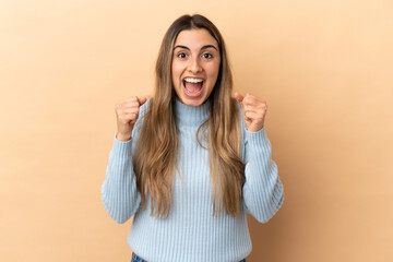 Young caucasian woman isolated on beige background celebrating a victory in winner position
