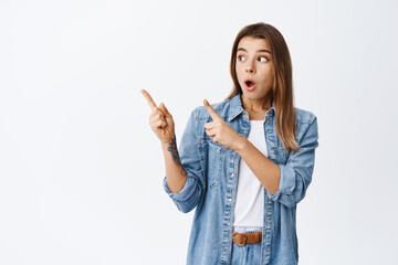 Young impressed woman with blond hair, drop jaw and gasping amazed while pointing at upper left corner, checking out advertisement on copy space, white background