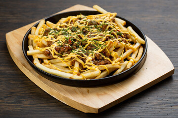 French fries with chopped beef in a metal frying pan on a wooden board. fried roll with meat and cheese sauce
