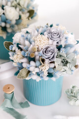 Bouquet with roses, hydrangea and spikelets in blue colors. Stabilized flowers in a blue ceramic vase at home on the dressing table. Interior decor.