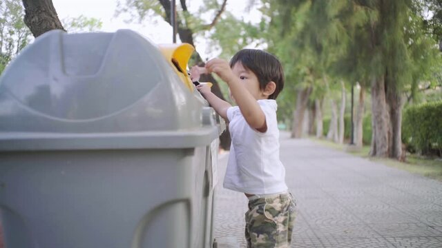 Little 2-3 year boy keep trash clean into park bin in nature public park environment concept