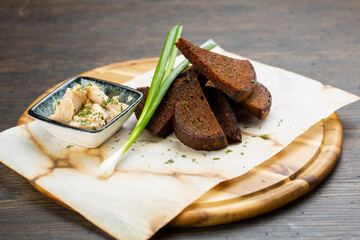 pate with black bread croutons with green onions on a wooden board