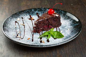 chocolate dessert with cherry filling and nuts. a slice of cake decorated with liquid chocolate and a mint leaf