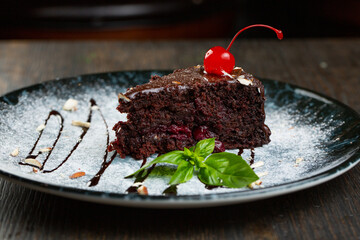 chocolate dessert with cherry filling and nuts. a slice of cake decorated with liquid chocolate and a mint leaf