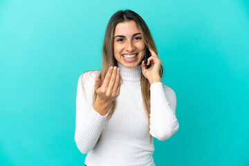 Young caucasian woman using mobile phone isolated on blue background inviting to come with hand. Happy that you came