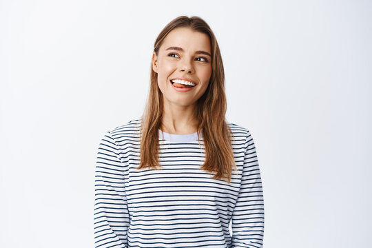 Portrait of healthy and happy young woman smiling, showing tongue and looking dreamy at upper left corner, imaging something with pleased face, white background