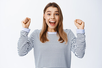 Image of excited blond woman winning and celebrating achievement, raising hands up and screaming...
