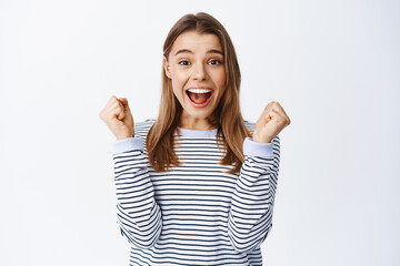 Portrait of excited and happy young woman say yes and making fist pump gesture to celebrate win,...