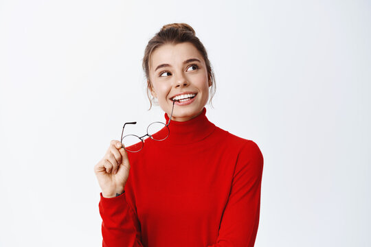 Portrait Of Smiling Happy Woman Thinking, Looking Up And Holding Glasses In Hands, Imaging Something, Having Interesting Thought, Standing Against White Background