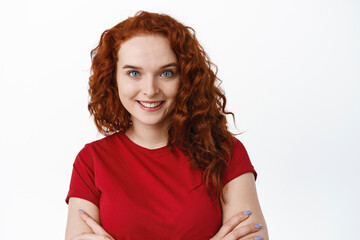 Close-up portrait of confident woman with ginger curly hair, cross arms on chest and smiling, have...