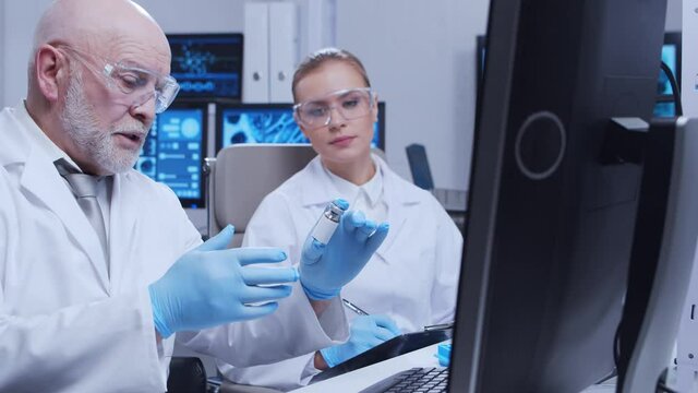 Elderly professor and young laboratory assistant are doing scientific experiment in a modern laboratory. Genetic engineers workplace. The concept of science, medicine and vaccine development.