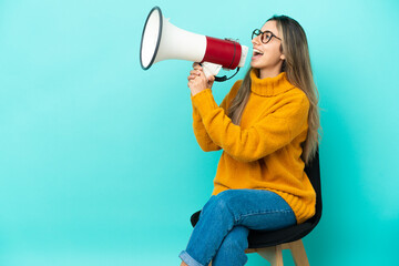 Young caucasian woman sitting on a chair isolated on blue background shouting through a megaphone