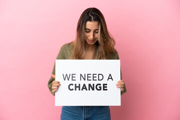 Young caucasian woman isolated on pink background holding a placard with text We Need a Change