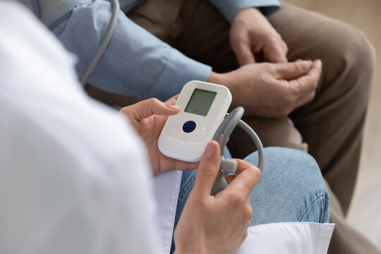 Crop close up of female nurse hold pulsimeter monitor measure high low blood pressure of elderly male patient. Woman doctor examine senior man check heartbeat heart rate. Geriatric concept.