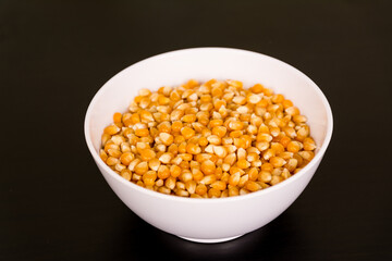 Heap of raw popcorn grains in round white bowl. Dry yellow corns seeds, maize or sweetcorn kernels