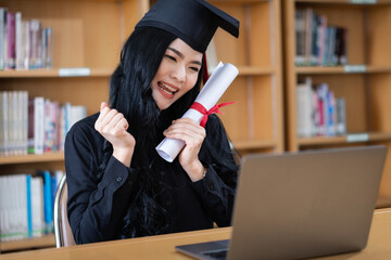 A young Asian female university graduate expressing joy and excitement to celebrate her achievement of degree graduation in front of a laptop making a remote video call to her parents at home