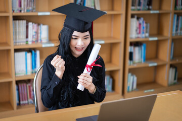 A young Asian female university graduate expressing joy and excitement to celebrate her achievement of degree graduation in front of a laptop making a remote video call to her parents at home