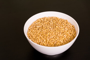 grains of wheal  in round white bowl on black table