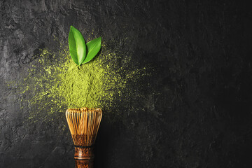 Matcha tea powder on dark background with whisk and leaves with copy space.