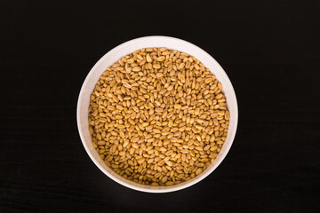 grains of wheal  in round white bowl on black table top view