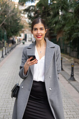 Beautiful businesswoman with mobile phone standing smiling on the street 