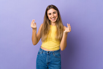 Young woman over isolated purple background making money gesture