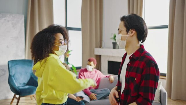 Close up of mixed race couple, a guy and a girl wearing masks greets each other with their elbows. Indoor mask party, 5 people together during quarantine coronavirus covid-19, the new normality