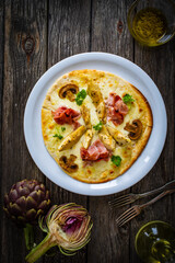 Pizza with artichokes, champignons, ham and mozzarella on wooden background
