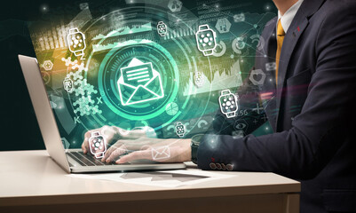 Business hand typing on a modern laptop with mailing icon coming out from multimedia screen, intuitive technology concept