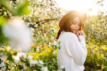 Young woman enjoying scent in blooming spring garden. The concept of youth, love, fashion and lifestyle.