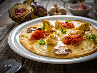 Pizza with artichokes, champignons, ham and mozzarella on wooden background
