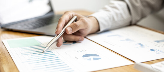 A close-up view of a businessman holding a pen pointing at a bar chart on a company financial...