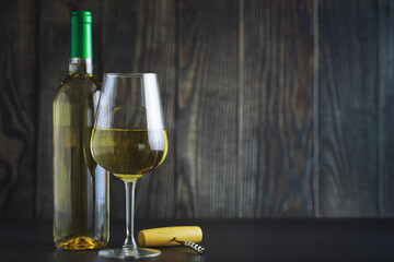 Transparent bottle of white dry wine on the table. White wine glass on a wooden background.