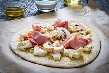 Uncooked pizza with artichokes, champignons, ham and mozzarella on wooden background