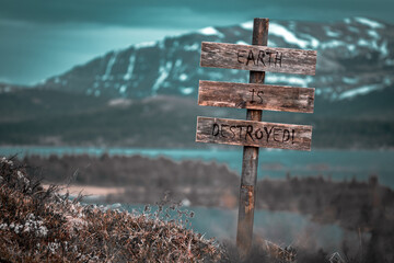 earth is destroyed text quote engraved on wooden signpost outdoors in landscape looking polluted and apocalyptic.