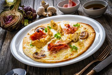 Pizza with artichokes, champignons, ham and mozzarella on wooden background

