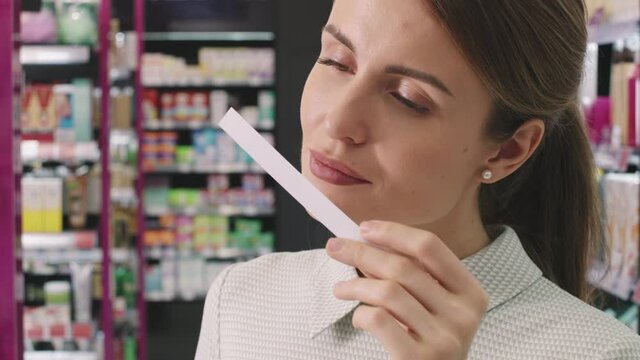 Slow-motion tilting-up closeup of attractive young caucasian woman spraying some perfume on blotter enjoying aroma standing in trendy beauty shop salon