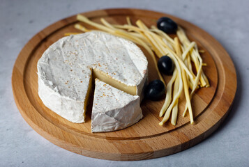 Assorted cheeses Camembert and smoked cheese with black grapes on stone background.