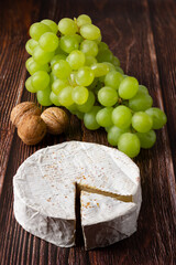 Camembert with green grapes and walnut on wooden table.