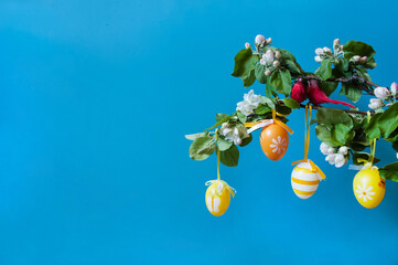 Easter composition. A branch of a blooming apple tree, cute red birds and colorful eggs close-up on a blue background. Happy Easter Holidays. Free space.