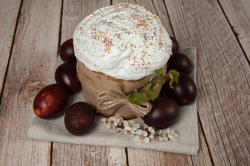 Easter composition. A blooming apricot branch, painted eggs and a glazed Easter cake decorated with sugar sprinkles close-up on a wooden background. Happy Easter Holidays. Selective focus.