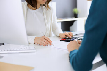 Accountant checking financial statement or counting by calculator income for tax form, hands close-up. Business woman sitting and working with colleague at the desk in office. Audit concept