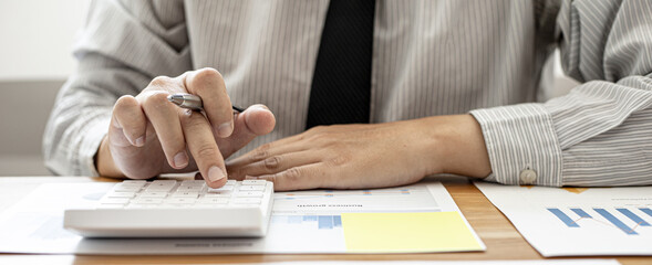 Close-up view A businessman using a calculator to calculate numbers on a company's financial...