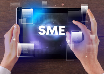 Close-up of a hand holding tablet with SME abbreviation, modern technology concept