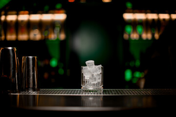 Gorgeous view of glass with ice standing on bar counter on blurred background - obrazy, fototapety, plakaty