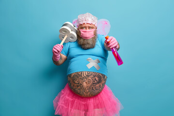 Funny bearded man with fat tattooed belly wears fairy costume protective mask holds detergent and...