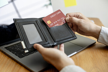 A businessman is pulling a credit card from his wallet in order to fill out the information, pay for the products to be ordered on the website on his laptop. Online shopping ideas.